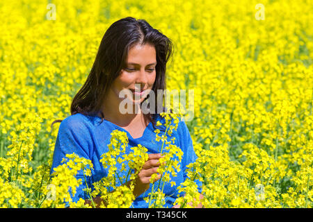 Young colombian woman looking at flower in blooming yellow rapeseed field Stock Photo