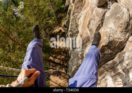 Climber's legs hanging on a rope in a harness, first person view from top to bottom. Stock Photo