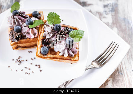 Belgian waffles with cream, jam, blueberries and mint leaves on a white plate. Close-up. Delicious Dessert Stock Photo