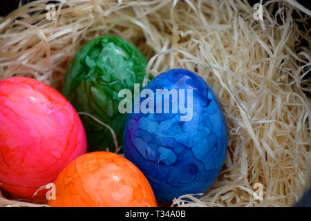 happy easter theme with colored eggs, easter basket filled with white straw and colored cooked eggs as easter background Stock Photo