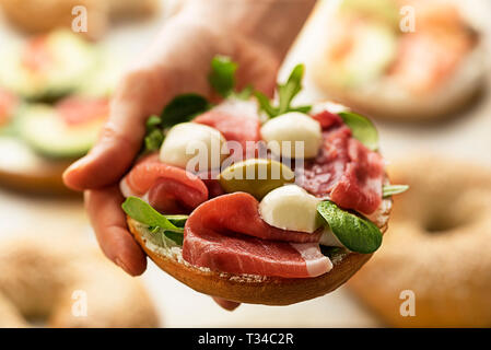 Woman is holding bagel sandwich with prosciutto and mozzareela cheese. Healthy food. Stock Photo