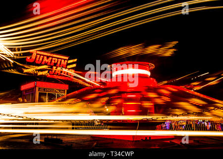 A thrilling fairground ride spins into a fiery vortex of light, its vivid lights blurring against the night sky in a dynamic long-exposure scene. Stock Photo