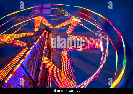 A thrilling fairground ride spins into a fiery vortex of light, its vivid lights blurring against the night sky in a dynamic long-exposure scene. Stock Photo