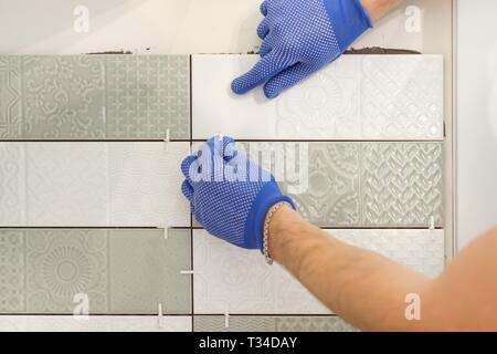 Installing ceramic tiles on the wall in kitchen. Placing tile spacers with hands, renovation, repair, construction. Stock Photo