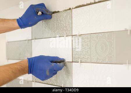 Installing ceramic tiles on the wall in kitchen. Placing tile spacers with hands, renovation, repair, construction. Stock Photo