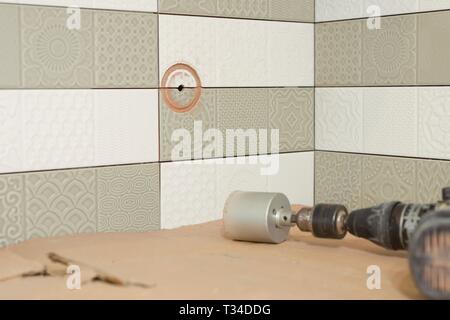 Preparatory work for the installation of an electrical outlet, building tools, tile cutter, grinder in the process of drilling tiles. Round hole in th Stock Photo