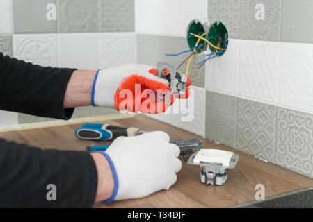 Renovation and construction in kitchen, close-up of electricians hand installing outlet on wall with ceramic tiles using professional tools. Stock Photo