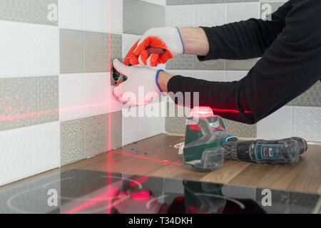Electrician using infrared laser level to install electrical outlets. Renovation and construction in kitchen. Stock Photo