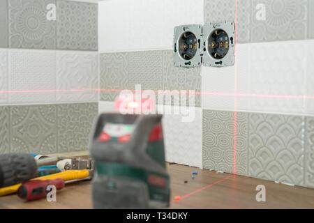 Electrician using infrared laser level to install electrical outlets. Renovation and construction in kitchen. Stock Photo