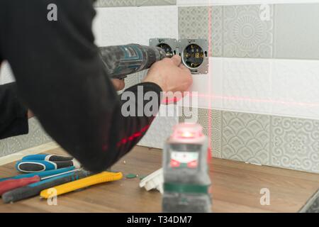 Electrician using infrared laser level to install electrical outlets. Renovation and construction in kitchen. Stock Photo