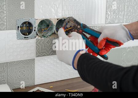 Renovation and construction in kitchen, close-up of electricians hand installing outlet on wall with ceramic tiles using professional tools. Stock Photo