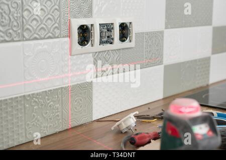 Electrician using infrared laser level to install electrical outlets. Renovation and construction in kitchen. Stock Photo