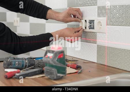 Electrician using infrared laser level to install electrical outlets. Renovation and construction in kitchen. Stock Photo
