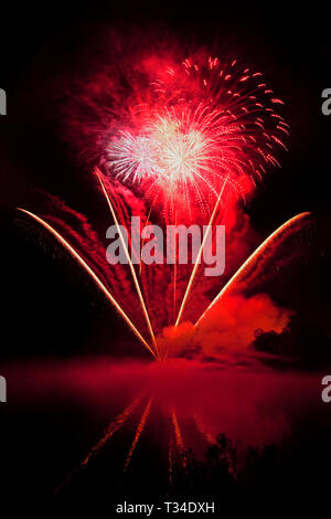 Spectacular commercial fireworks light up the sky with vibrant colour refelctions in a foreground lake - artistic light pattern. Stock Photo
