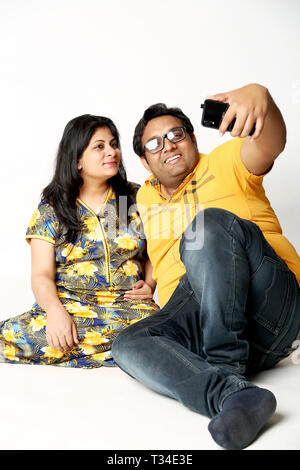 Couple is clicking selfie in the smartphone with sitting on the floor. Isolated on the white background. Stock Photo