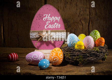 Colorful painted happy easter greeting card eggs in birds nest basket on rustic wooden old  background Stock Photo