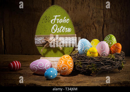 German greetings Frohe Ostern ( english translation happy easter ) Colorful painted eggs in birds nest basket on rustic wooden old  greeting card back Stock Photo