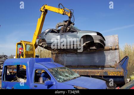 Crane with claw move an old crushed car from junkyard at car press crusher for recycling Stock Photo