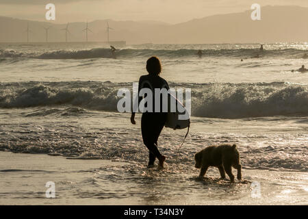 Silhouette of a female surfer walking in the surf with her dog, Bilbao, Spain Stock Photo