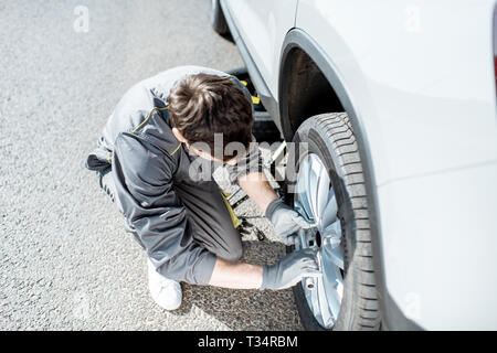 Worker unscrewing car wheel on the road, view from above Stock Photo