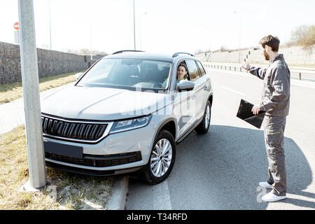 Road assistance worker helping young woman to get out from the roadside after the accident on the highway Stock Photo