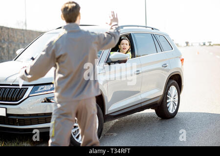 Road assistance worker helping young woman to get out from the roadside after the accident on the highway Stock Photo