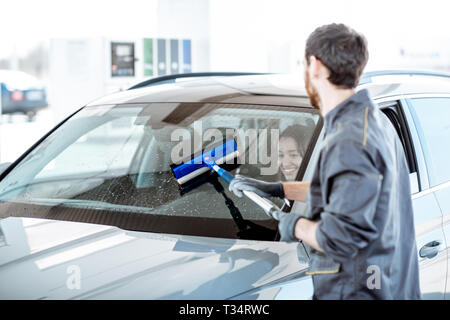 Gas station worker in uniform washing car windshield at the station Stock Photo