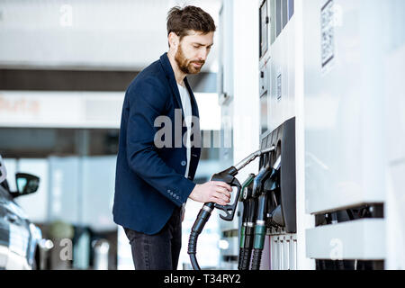 Businessman refueling his luxury car holding filling gun at the gas station Stock Photo