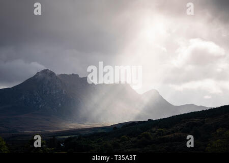 Rays of sunlight pierce the cloud to illuminate Ben Loyal, as seen from the A836 in Lairg, Northern Scotland. Stock Photo