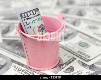 A bundle of US dollars in a metal pink pail on a set of dollar bills. The concept of abundance and excess cash Stock Photo