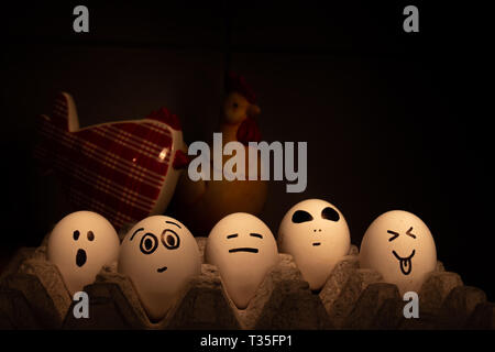 Several eggs with funny faces. They are watched over by two chickens out of focus. Conceptual image Stock Photo