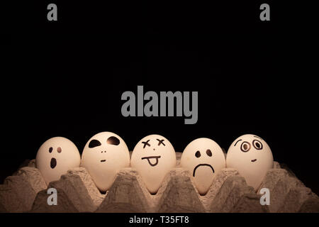 Chicken or Easter eggs with funny faces on black background. Stock Photo