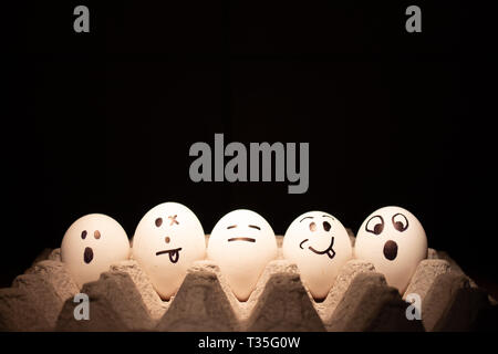 Chicken or Easter eggs with funny faces on black background. Stock Photo
