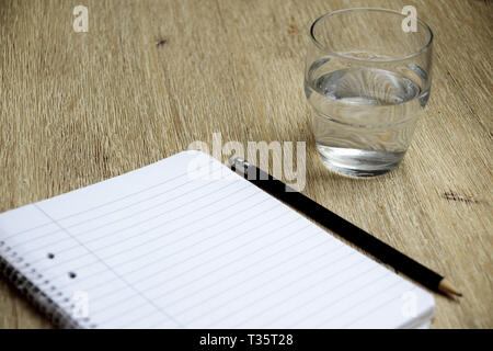 Notebook, pencil and glass of water on wooden table Stock Photo