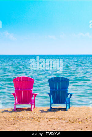 two plastic beach chairs by the sea capturing gender stereotyped colours of pink and blue Stock Photo