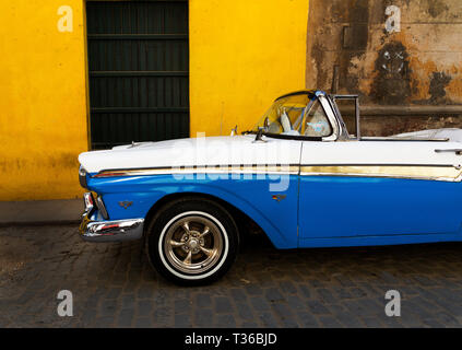 Blue and White 1957 Ford Fairlane 500 Sunliner Convertible parked on cobblestone street with yellow background wall in Havana, Cuba Stock Photo