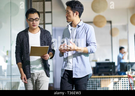 two young asian colleagues discussing business while walking in office. Stock Photo