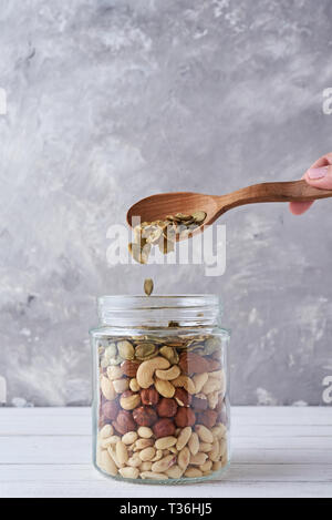 Different types of nuts and seeds in glass jar with wooden spoon, close up Stock Photo