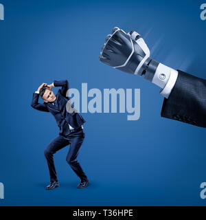 Businessman covering his head with hands to protect himself from big robot hand in suit. Stock Photo