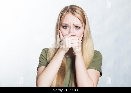 Surprised beautiful young woman covers mouth in shock Stock Photo