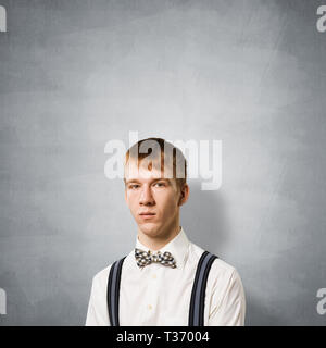 Boy having serious and calm face. Caucasian redhead student has confident facial expression. Portrait of stylish guy wears white shirt, bow tie and su Stock Photo