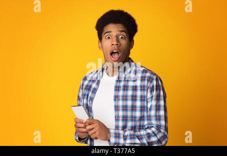 Shocked guy holding phone, astonished by social media online news Stock Photo