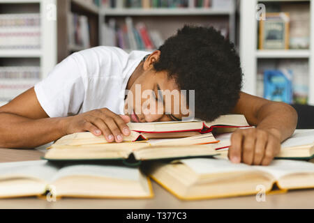 Tired guy napping on books stack in library Stock Photo