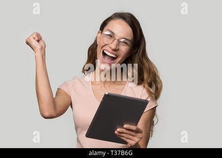Happy woman in glasses holding digital tablet screaming celebrating win Stock Photo