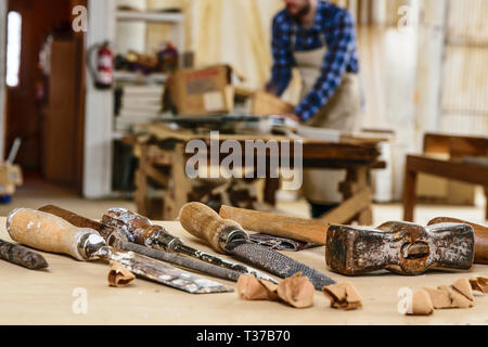 Carpenter working with hammer and chisel on wood table. Workshop background. Stock Photo
