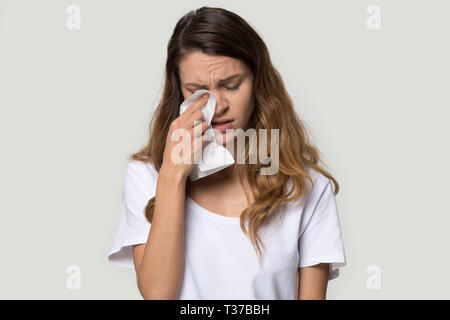 Unhappy young woman holding tissue wiping tears studio shot Stock Photo