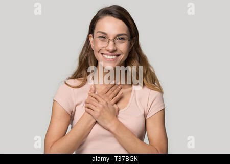 Headshot woman in glasses feels grateful holding hands on chest Stock Photo