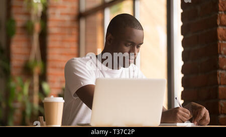 Serious african american man working studying with laptop making notes Stock Photo