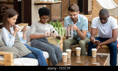 Diverse young friends using social media on phones in cafe Stock Photo