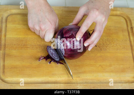 Close up of female slicing ends off of a red onion on a cutting board. Stock Photo